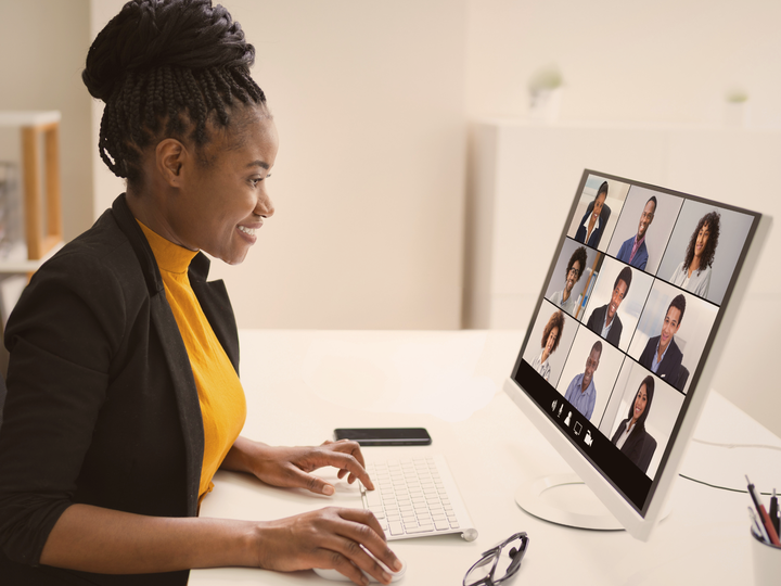 A woman faces a computer screen on a desk during a video conference call.