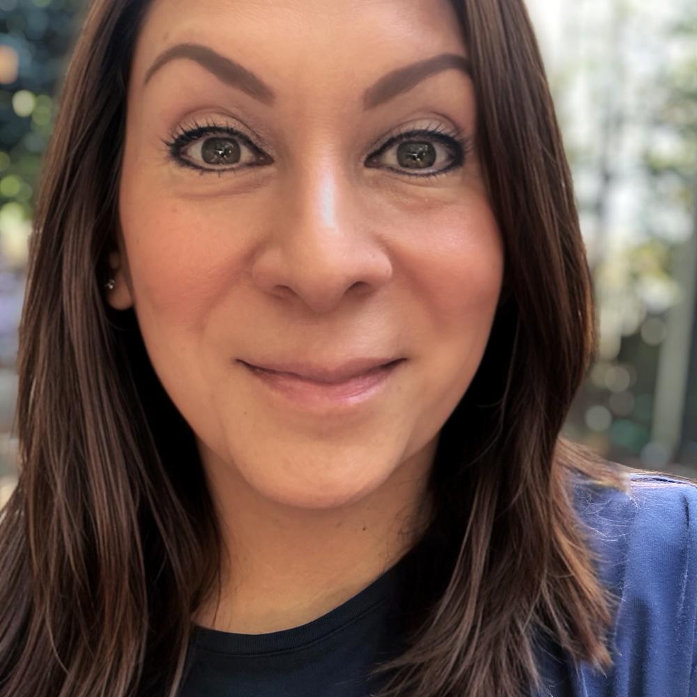 Brunette woman in a navy blue shirt smiling outdoors. 